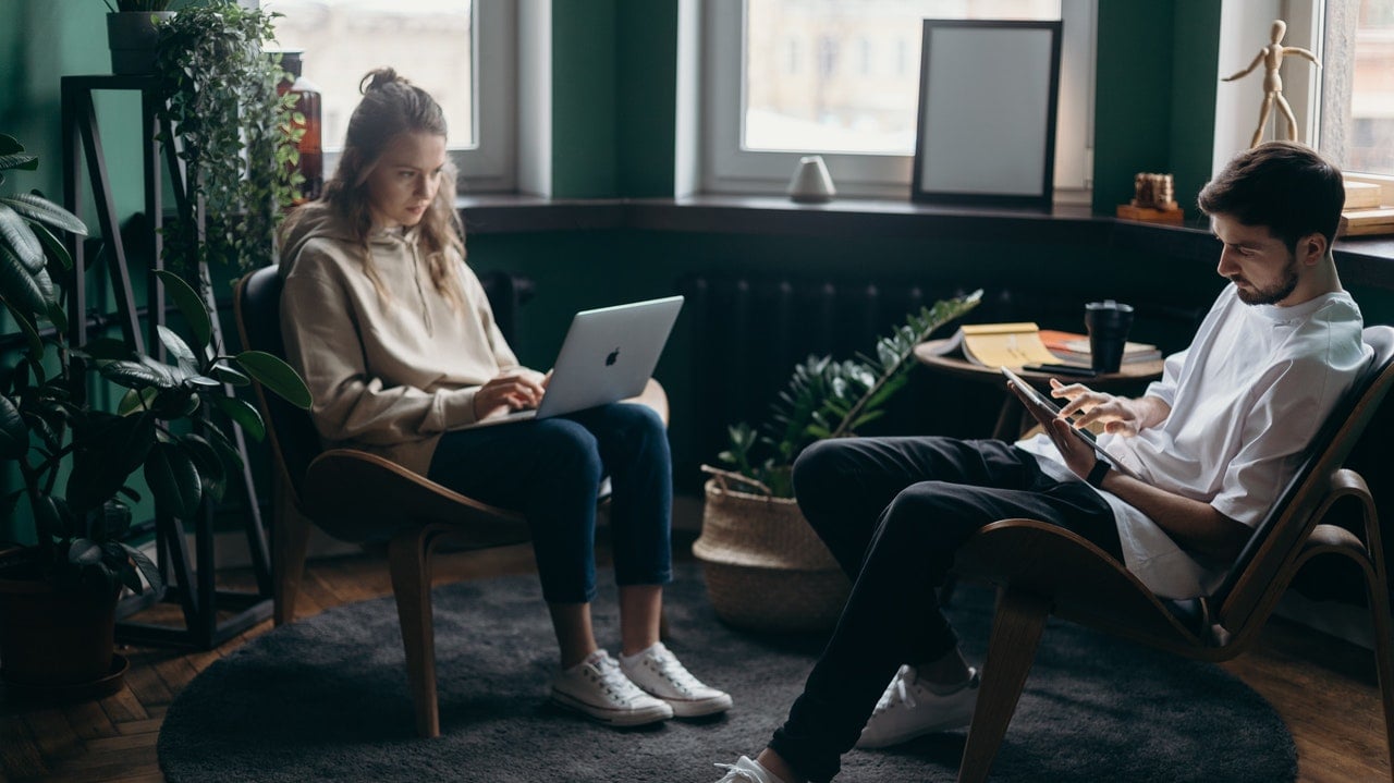 Two people sitting in a well-decorated living room working on laptops
