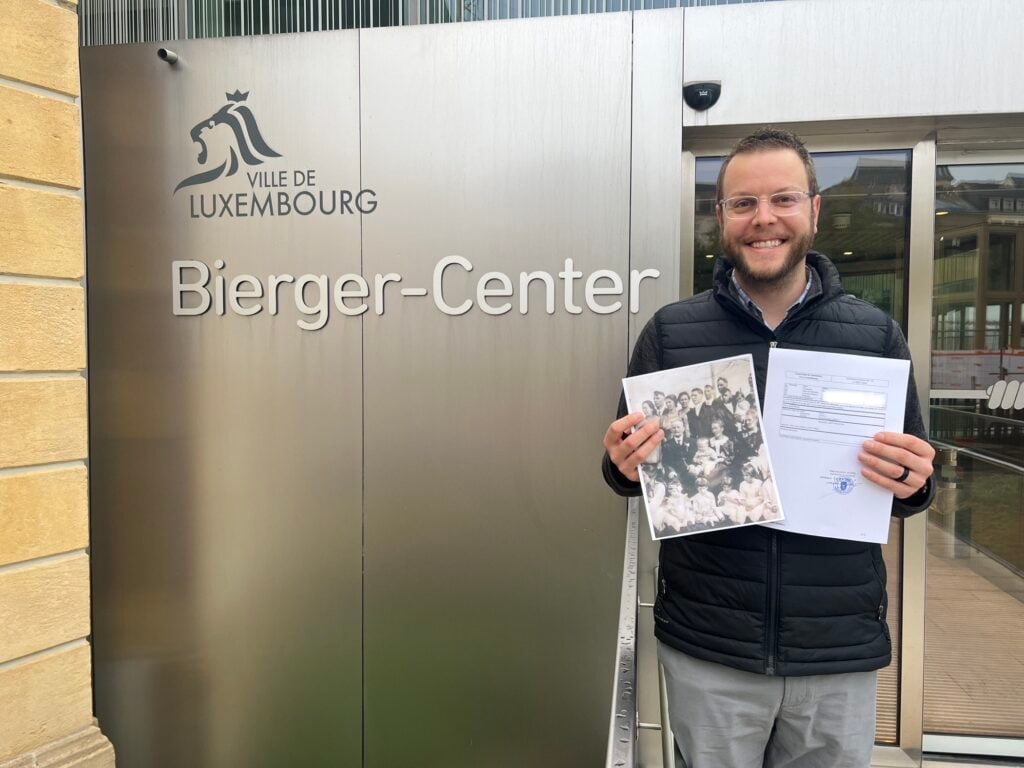 Smiling newly accepted Luxembourg dual citizen outside of Bierger-Center holding up official certification papers
