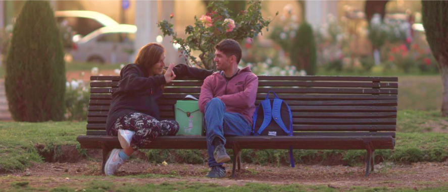 Two Luxembourgers smiling, sitting on a bench in conversation.