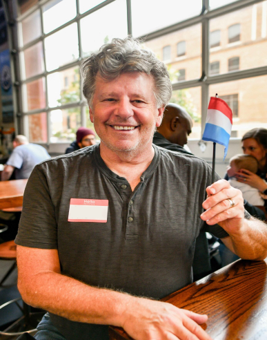 Man smiling, holding Luxembourg flag and sitting at a table.
