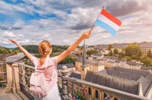 Woman on a terrace overlooking Luxembourg City, wearing a backpack and waving a Luxembourg flag